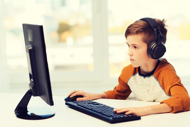concepto de ocio, educación, niños, tecnología y personas - niño con computadora y auriculares escribiendo en el teclado o jugando videojuegos en casa