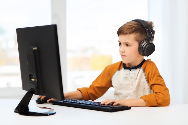 concepto de ocio, educación, niños, tecnología y personas - niño feliz con computadora y auriculares escribiendo en el teclado o jugando videojuegos en casa