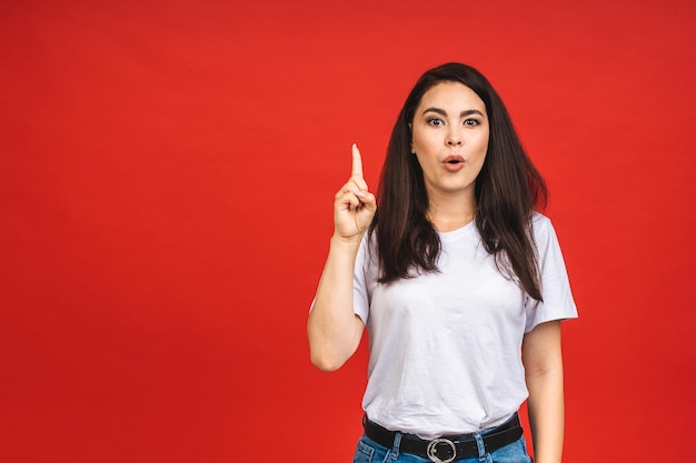 Concepto de ocio y estilo de vida de la gente joven Moda hermosa joven sorprendida estudiante caucásica joven vistiendo ropa elegante riendo señalando con el dedo hacia arriba Aislado sobre fondo rojo