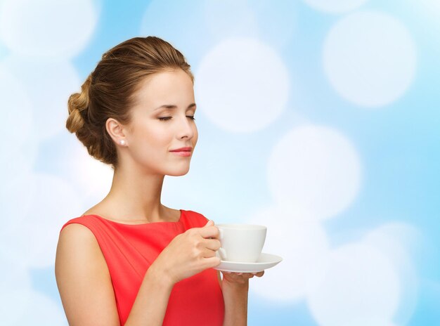 concepto de ocio, felicidad y bebida - mujer sonriente vestida de rojo con una taza de café sobre fondo de luces azules