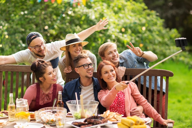 concepto de ocio, fiesta, tecnología, gente y vacaciones - amigos felices tomando fotos con un selfie de smartphone y reuniéndose para cenar en la fiesta del jardín de verano