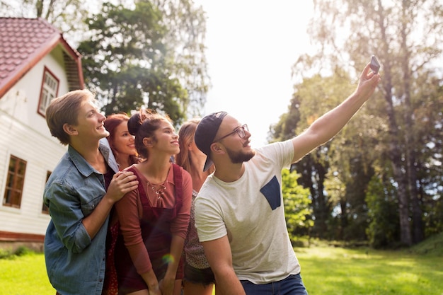 Foto concepto de ocio, fiesta, tecnología, gente y vacaciones - amigos felices tomando selfie con smartphone en el jardín de verano