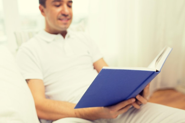 concepto de ocio, información, personas y medios de comunicación: cierre de un hombre feliz leyendo un libro en casa