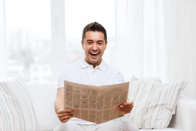 concepto de ocio, información, personas y medios de comunicación - hombre feliz leyendo el periódico y riéndose en casa