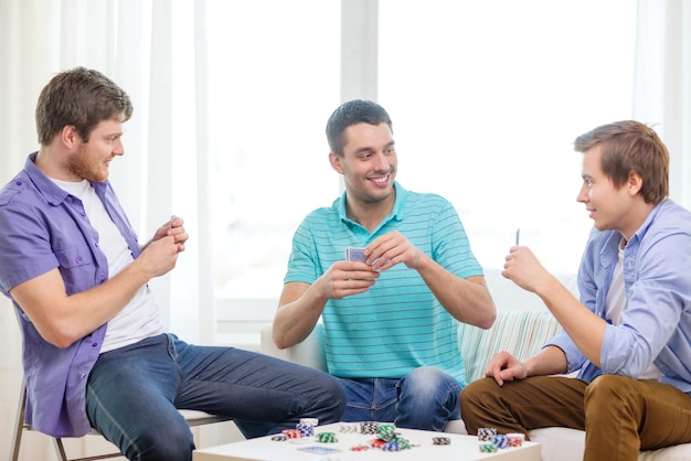 concepto de ocio, juegos y estilo de vida - felices tres amigos varones jugando al póquer en casa