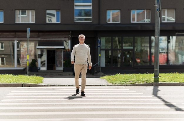 concepto de ocio y personas - hombre mayor caminando por el cruce de peatones de la ciudad de verano