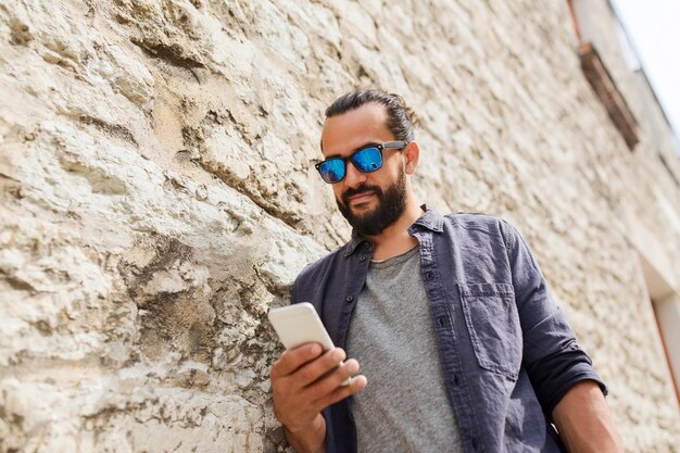 concepto de ocio, tecnología, comunicación y personas - hombre con gafas de sol enviando mensajes de texto en un smartphone en un muro de piedra