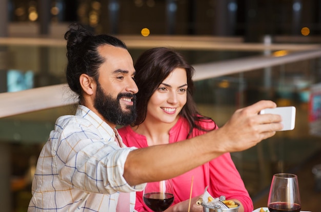 Foto concepto de ocio, tecnología, fecha, gente y vacaciones - pareja feliz cenando y tomando selfie por teléfono inteligente en el restaurante