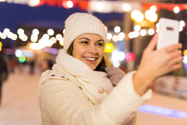 Concepto de ocio y tecnología de invierno de Navidad mujer joven feliz tomando fotografías con el teléfono inteligente en