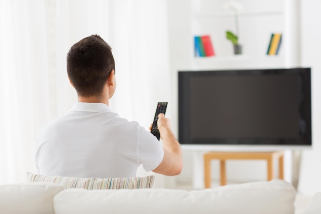concepto de ocio, tecnología, medios de comunicación y personas - hombre viendo televisión y cambiando canales en casa desde atrás