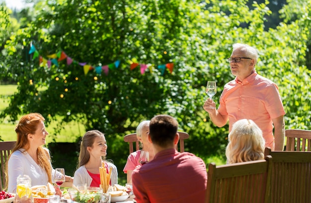 concepto de ocio, vacaciones y personas - familia feliz teniendo una cena festiva o una fiesta de verano en el jardín y celebrando