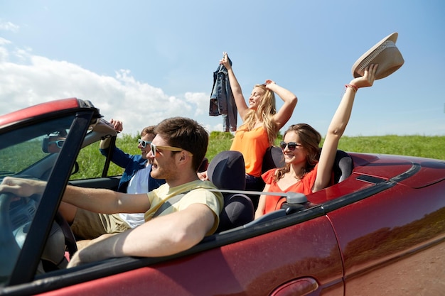 concepto de ocio, viaje por carretera, viajes y personas - amigos felices conduciendo en un coche cabriolet en el campo y saludando con la mano