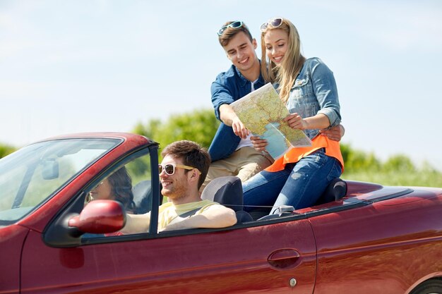 concepto de ocio, viaje por carretera, viajes y personas - amigos felices con mapa conduciendo en camión cabriolet a lo largo de la carretera rural y buscando ubicación