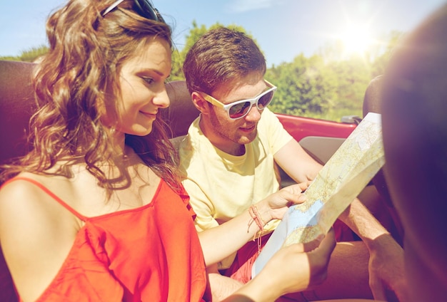 concepto de ocio, viaje por carretera, viajes y personas - amigos felices con mapa conduciendo en camión cabriolet a lo largo de la carretera rural y buscando ubicación