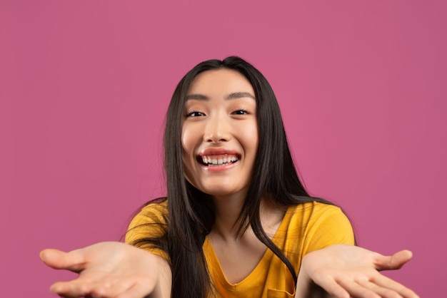 Concepto de oferta genial dama asiática feliz con las palmas abiertas mirando a la cámara y sonriendo posando sobre violeta