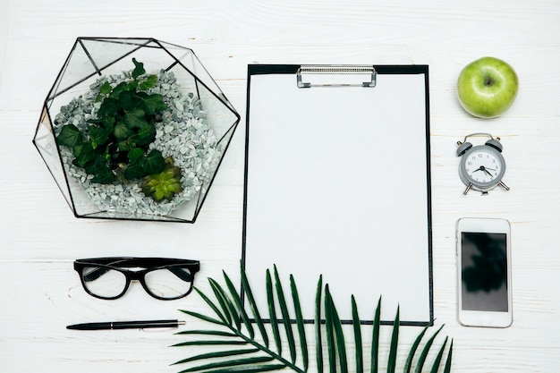 Concepto de oficina. Jarrón Florarium, Bloc de notas, gafas y teléfono sobre un fondo blanco.