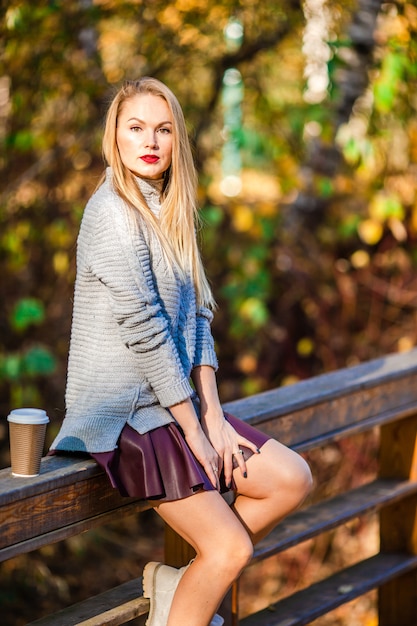 Concepto de otoño - hermosa mujer tomando café en el parque de otoño bajo el follaje de otoño