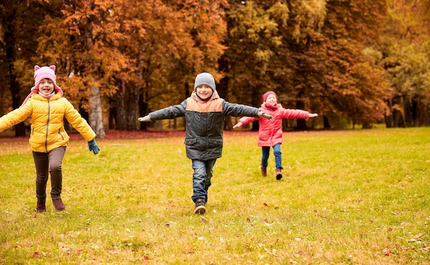 concepto de otoño, infancia, ocio y personas - grupo de niños pequeños felices corriendo y jugando aviones al aire libre