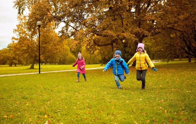 concepto de otoño, infancia, ocio y personas - grupo de niños pequeños felices jugando al juego de etiquetas y corriendo en el parque al aire libre