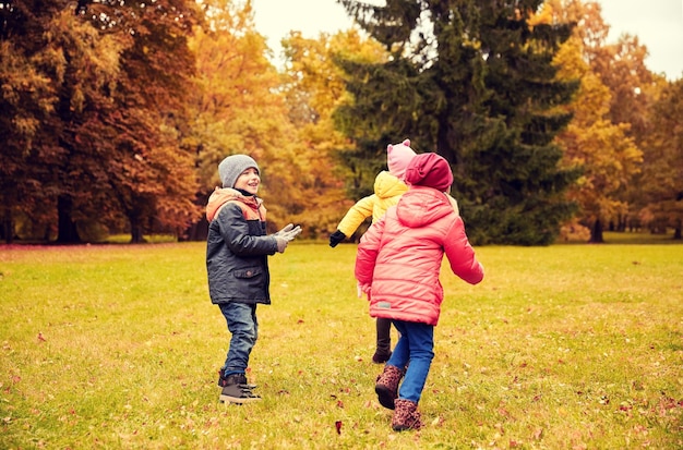 concepto de otoño, infancia, ocio y personas - grupo de niños pequeños felices jugando al juego de etiquetas y divirtiéndose en el parque al aire libre