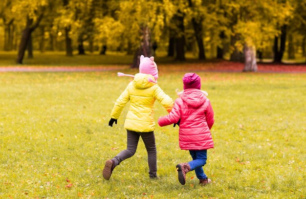 concepto de otoño, infancia, ocio y personas - niñas felices jugando al juego de etiquetas y corriendo en el parque al aire libre