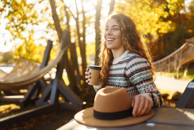 Concepto de otoño mujer bebiendo café en un banco contra el telón de fondo del lago disfrutando de la soledad con la naturaleza