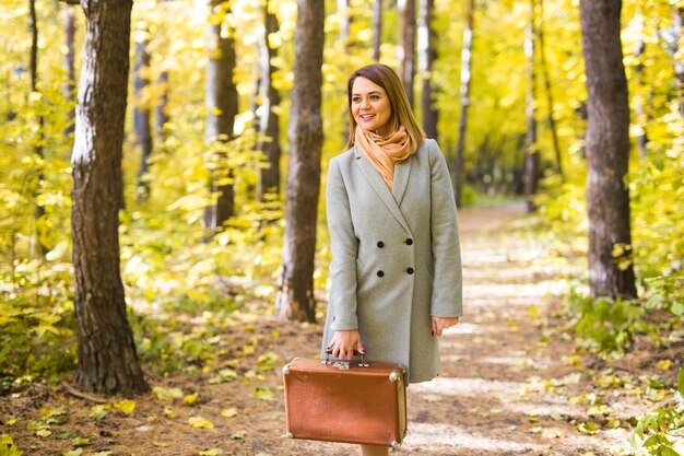 Concepto de otoño, naturaleza y personas - mujer hermosa joven caminando en el parque con maleta