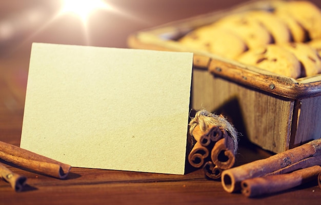 concepto de panadería, culinaria, vacaciones y comida - primer plano de una tarjeta de felicitación en blanco con galletas de avena en una caja de madera y canela en la mesa