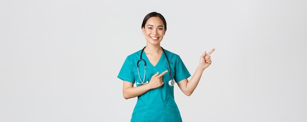 Concepto de pandemia de trabajadores de la salud de covid sonriendo hermosa mujer asiática enfermera pasante señalando el dedo ...