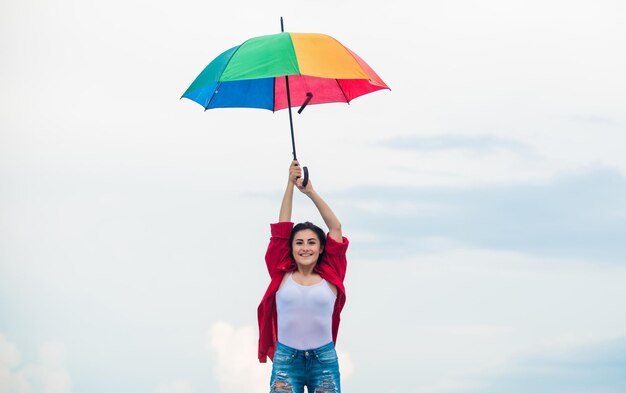 Concepto de paracaídas Buen clima Caída de bienvenida Mujer bonita con paraguas colorido Paraguas arcoíris Clima lluvioso Buen humor Buenas vibraciones Persona de mente abierta Chica sintiéndose bien fondo del cielo