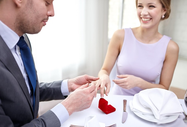 Foto concepto de pareja, amor, compromiso y vacaciones - cerca del hombre poniendo el anillo en el dedo de su prometida en el restaurante