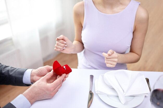 concepto de pareja, amor, compromiso y vacaciones - cerca de una joven emocionada y un novio dando su anillo en el restaurante