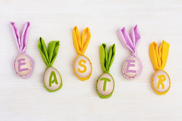 Concepto de Pascua divertido Letras multicolores Pascua y huevos de madera con orejas de tela como conejito divertido