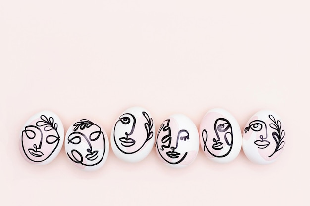 Concepto de Pascua feliz Caras surrealistas en huevos sobre fondo rosa Estilo de arte y en línea Vista superior Endecha plana Espacio de copia