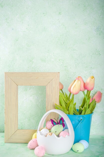 Concepto de Pascua feliz con huevos de Pascua en canasta y flores de primavera. Fondo de Pascua con espacio de copia y marco de fotos