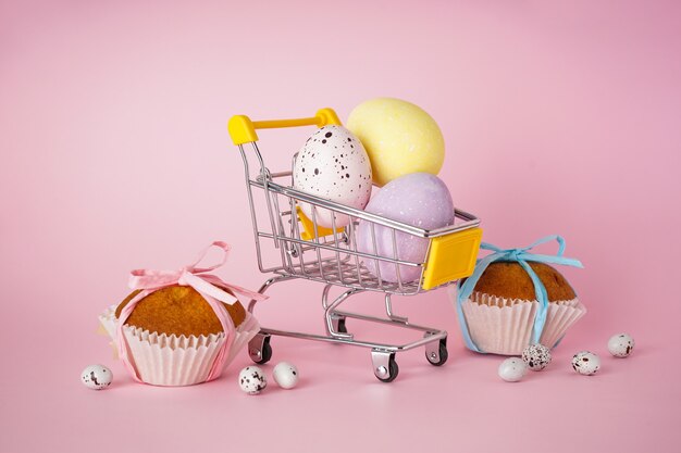 Concepto de Pascua feliz. Pastel de Pascua y huevos de Pascua en un carro con flores sobre un fondo rosa.