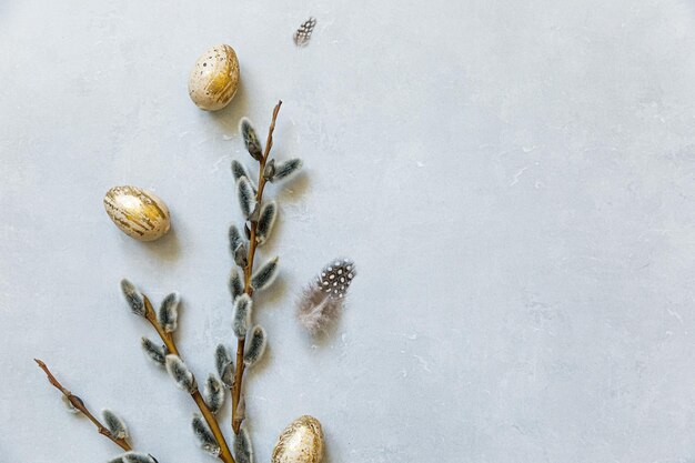 Concepto de Pascua feliz. Preparación para vacaciones. Pluma de sauce de huevos de Pascua decorados dorados sobre fondo gris piedra de hormigón. Minimalismo simple, plano, vista superior, copia espacio.