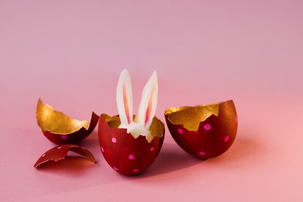 Concepto de pascua. Huevos de colores sobre fondo rosa, conejito de Pascua escondido