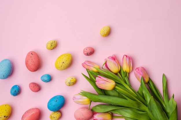 Concepto de Pascua, huevos multicolores y ramo de tulipanes se encuentran en una mesa de color rosa blanco. - Copia espacio