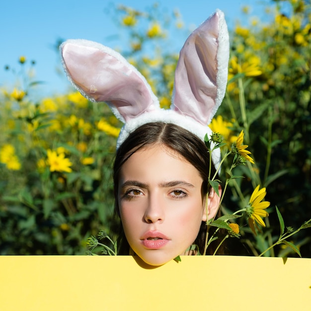 Concepto de Pascua mujer joven con orejas de conejo y mirando a escondidas sobre un tablero de anuncios hermosa mujer joven