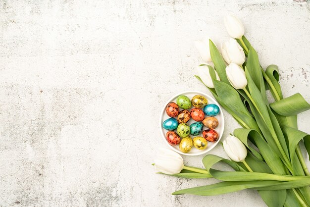 Concepto de Pascua y primavera. Vista superior de tulipanes blancos y huevos de pascua de colores sobre fondo de hormigón