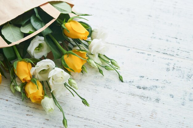 Concepto de Pascua Ramo de rosas blancas y amarillas frescas en bolsa de papel sobre fondo de madera blanca vieja Concepto de celebración de Pascua Pesah Concepto del día de la madre Fondo de primavera del día de la mujer Vista superior