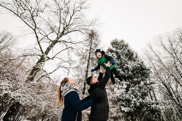 Concepto de paternidad, moda, temporada y personas - familia feliz con niño en ropa de invierno caminando al aire libre en el parque. El concepto de celebrar una Feliz Navidad.