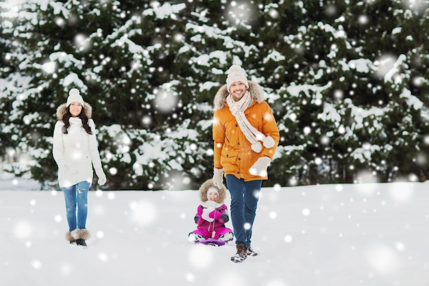 concepto de paternidad, moda, temporada y personas - familia feliz con un niño en trineo caminando en el bosque de invierno