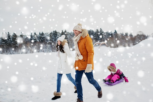 concepto de paternidad, moda, temporada y personas - familia feliz con un niño en trineo caminando en invierno al aire libre