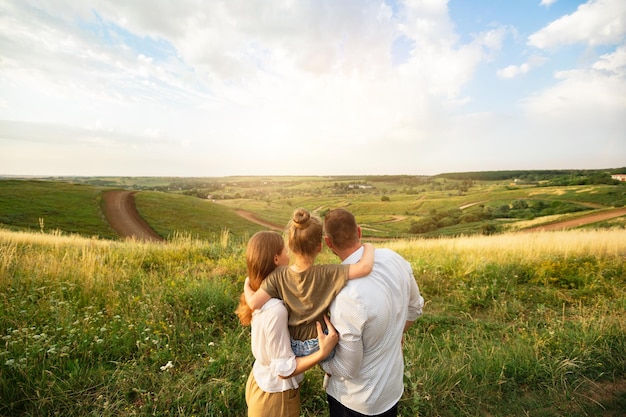 Concepto de paternidad. Retrato de vista trasera de la familia feliz con niño en las manos, de pie en medio del campo