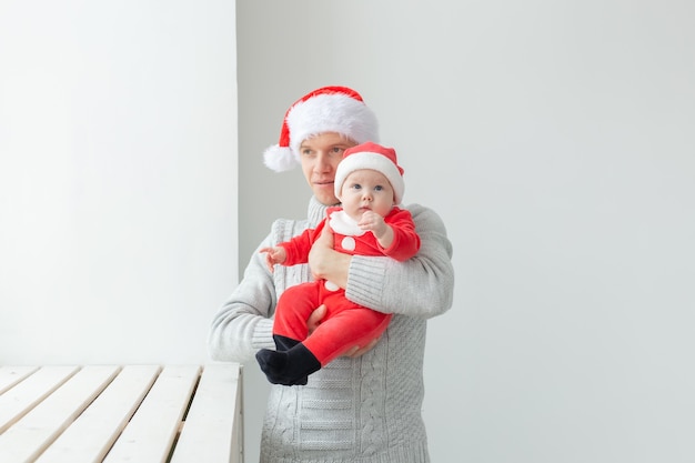 Concepto de paternidad y vacaciones - Padre con su bebé con gorro de Papá Noel celebrando la Navidad