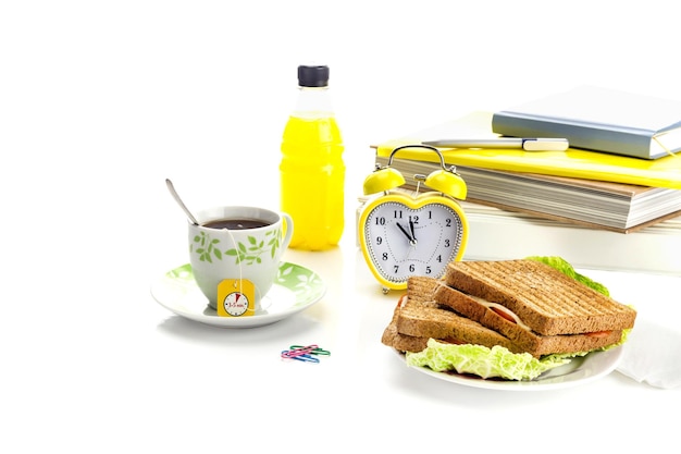 El concepto de una pausa para el almuerzo en un instituto escolar o en el lugar de trabajo Brindis en un plato una taza de té y un reloj en un primer plano de fondo blanco