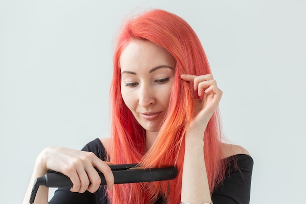 Concepto de peinado, peluquería y personas - elegante mujer pelirroja con rizador en pared blanca.