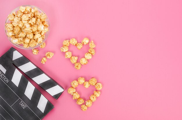 Concepto de película de San Valentín. Claqueta de cine con corazones de palomitas de caramelo con espacio de copia sobre un fondo rosa.